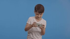 Little boy plays video game on his cell phone. Blue background studio. People pose using gamer isolated on lifestyle concept. Slow motion video. 