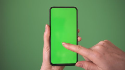 Phone in the hand close up isolated at green background. Phone screen is green chroma key, background chroma key green screen