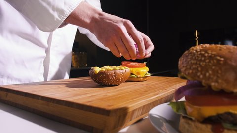 Chef Making Burger With Meat Cutlet, Cheese, Tomato, Onion In Fast Food Restaurant Kitchen. Cooking Delicious Hamburgers For Dinner In Cuisine. Person Prepare Meal In Kitchen. Fast Food Dish Close up.