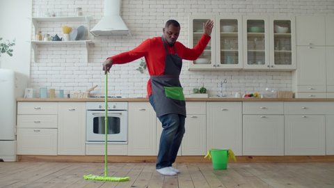 Optimistic black male dancing with mop during cleanup