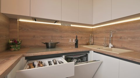 Closeup panorama of modern white and wooden beige kitchen interior/ some drawer pulled out, dishwasher door open, flat profile shot.