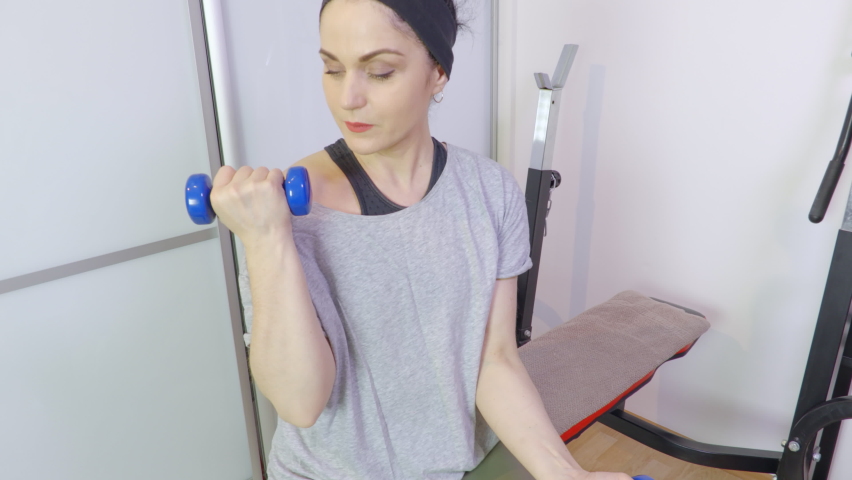 Sporty woman on fitness bench doing exercise for biceps