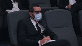 man in medical mask taking notes in notebook at conference
