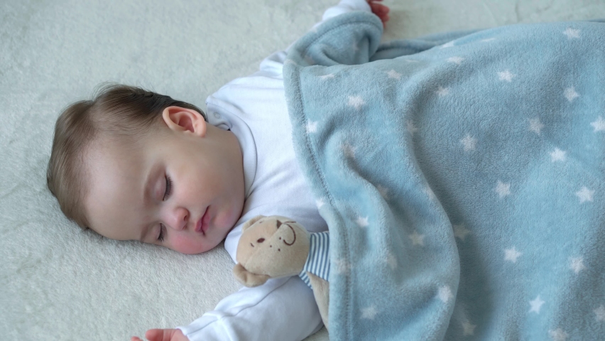 Authentic close up of cute caucasian little infant chubby baby girl sleep sweetly in comfortable white and blue bed with teddy bear. Child care, Sleeping kid, Childhood, Parenthood, life concept | Shutterstock HD Video #1068918956