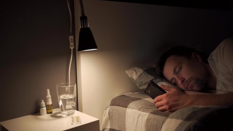 Guy with sore and tired eyes when using gadget at night, sleeplessness, sleep disturbance, blue light screen spoils sleep schedule. Man addicted to internet, social media and chatting on smart phone