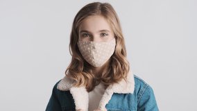 Pretty blond teenage girl wearing protective mask preening on camera isolated on yellow background. Safety first concept