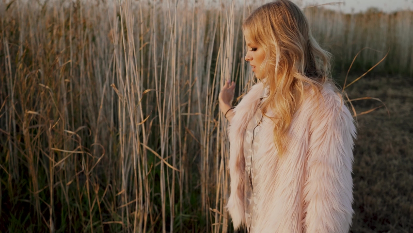 Pretty young woman walks through field and dreams, inspired look. Portrait of a woman walking through the autumn field and touching her reeds with hand. 4k