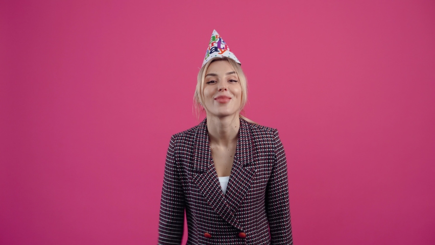 The happy young woman who celebrates her birthday, wears a cone on her head Beautiful young mature blonde in pink jacket. Isolated on a pink background. Concept of life. People