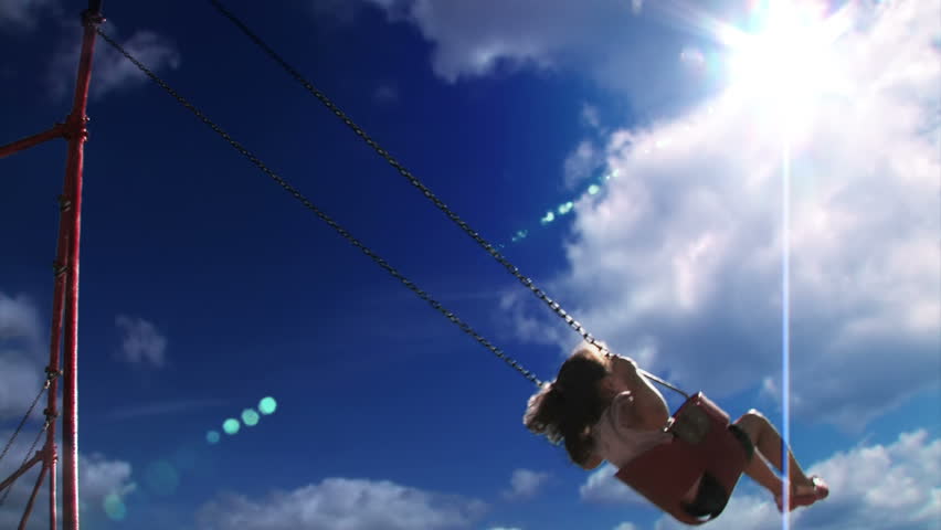 A young girl swings on a swing set in a playground  Low angle with the sky shown