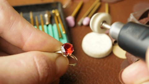 A professional jeweler polishes a red gem on a gold ring using a special tool. A professional engraver polishes the ring with a felt tip. 