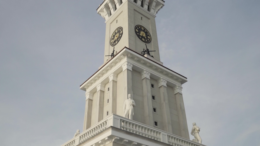 Bottom view of a clock tower with a long spire on blue cloudy sky background. Action. Details of an ancient historical building.