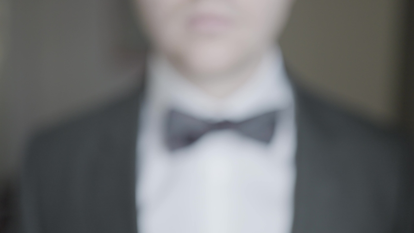 Close-up of gentleman adjusting bow tie. Action. Attractive man epicly adjusts bow tie on suit. Gentleman gracefully and courageously adjusts bow tie Royalty-Free Stock Footage #1068935036