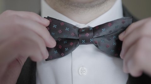 Close-up of gentleman adjusting bow tie. Action. Attractive man epicly adjusts bow tie on suit. Gentleman gracefully and courageously adjusts bow tie
