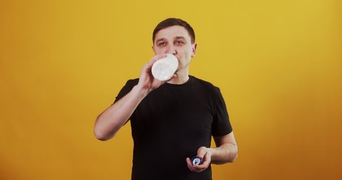 Portrait of young man drinking milk from the bottle over yellow background. He has a bottle of fresh milk in his hands
