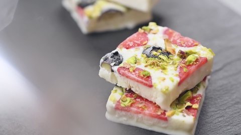 Hand takes a piece of frozen yogurt bark with strawberries, blueberries and pistachios. 