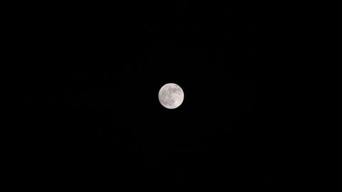 Bright full moon set against dark black sky at night in slow motion