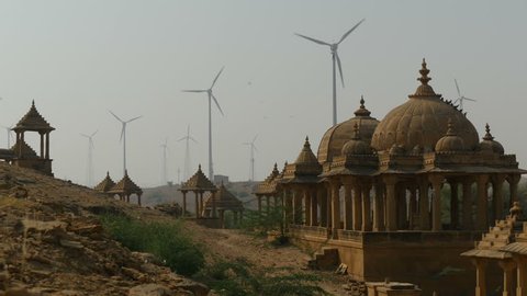 A large wind farm is visible behind ancient historical buildings nearby Jaisalmer, India.