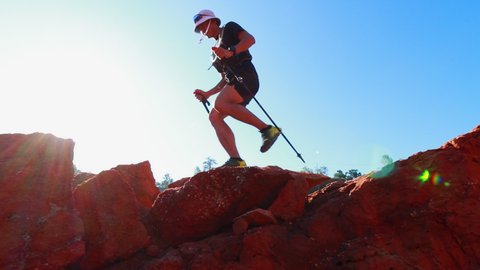 man trail runner climb rock using trekking poles