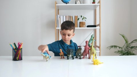 Focused kid playing with dinosaurs at home. Boy learning paleontology by dino toys at leisure. Concept of clever child and early education