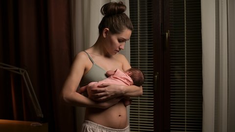 Breastfeeding a newborn baby, a woman holds her son in her arms and feeds him in the evening at home