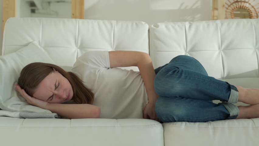 Women have abdominal pain because of menstruation. She was lying in sofa and holding her stomach. | Shutterstock HD Video #1068955847