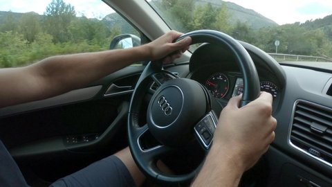 Cantabria, Spain - August 31, 2020: SLOW MOTION SHOT - Close-Up hands on car steering wheel. Man driving a car to journey road trip in summer vacation.