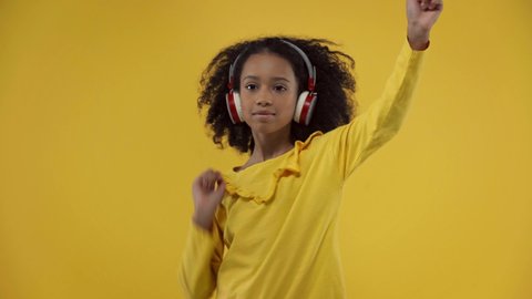 african american kid listening music and dancing isolated on yellow