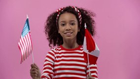 african american kid with usa and canadian flags isolated on pink