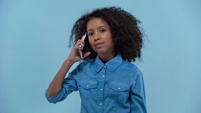 smiling african american kid talking on smartphone isolated on blue