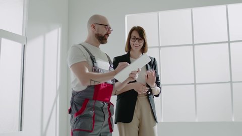 Skilled designer in grey jumpsuit presents elegant renovation of spacious flat to lady realtor in glasses in room slow motion