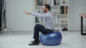 side view of businessman in formal wear doing sit ups on fitness ball in office