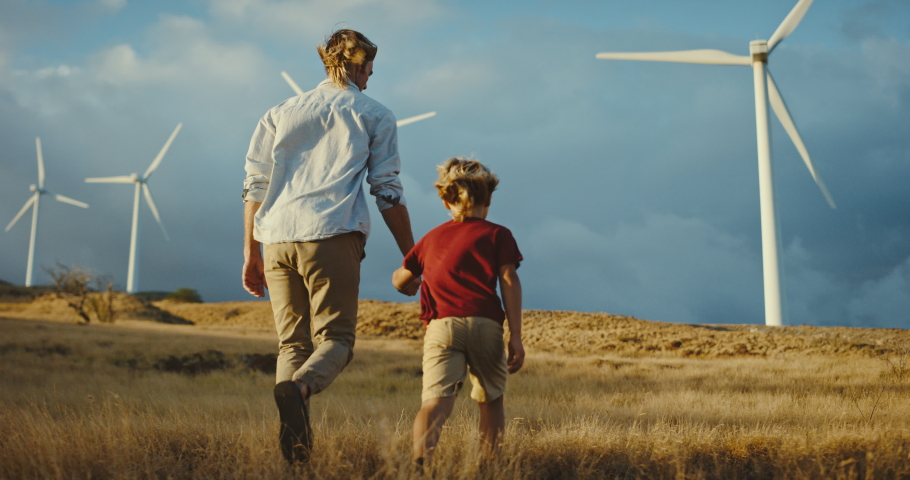 Father and son walking towards white windmills on a golden hill at sunset, walking to a cleaner and promising future, sustainability for future generations, father and son family lifestyle Royalty-Free Stock Footage #1068963409