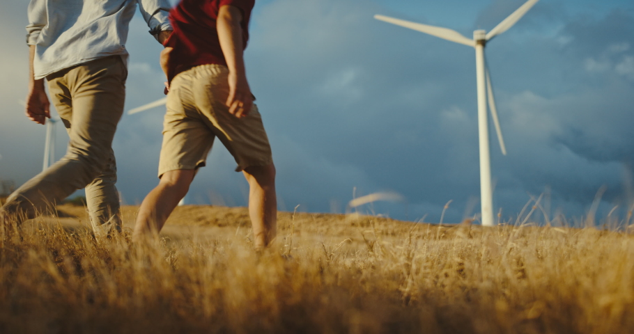 Father and son walking to windmills on golden hill at sunset, family lifestyle, clean energy wind turbines, future generations and clean sustainable energy | Shutterstock HD Video #1068963418