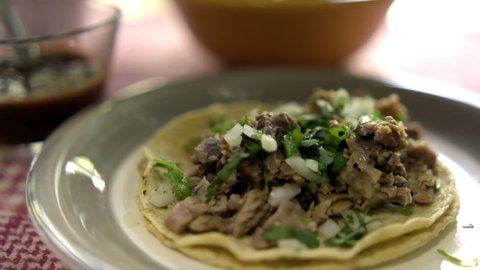 Close-up of tasty beef barbacoa taco with chopped coriander and onion on white plate. Authentic chopped beef meat taco above white and red checkered tablecloth. Classic Mexican food