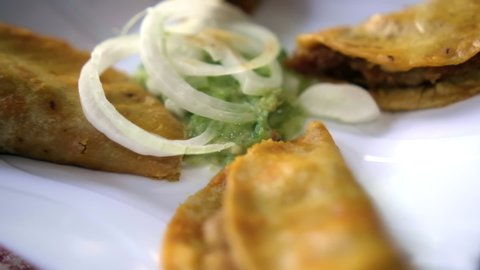 Close-up of tasty basket tacos on white plate with green sauce and onion slices in the middle. Authentic steamed canasta tacos above white and red checkered tablecloth. Classic Mexican food
