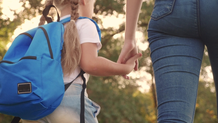 Mom and daughter go to school. happy family education concept. schoolgirl with mom and daughter go hand in hand to school on footpath in the park. lifestyle little girl with a briefcase time to study | Shutterstock HD Video #1068966781
