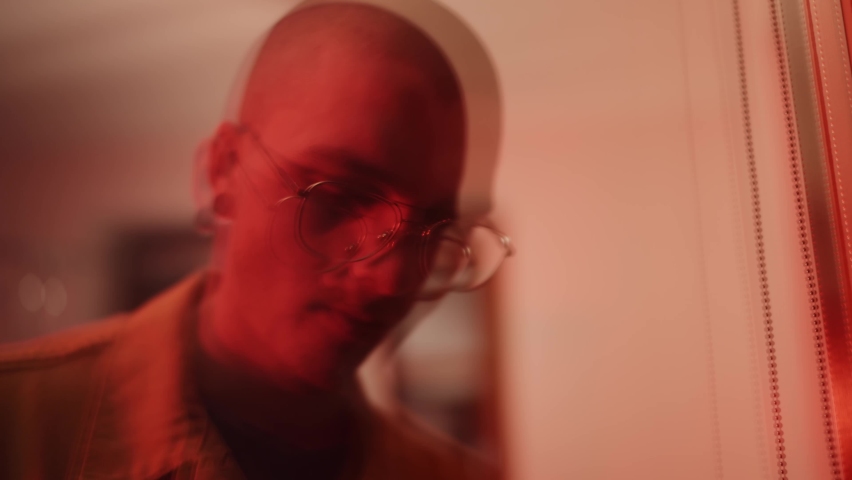 Young, depressed man looking out the window. Reflection of a sad, isolated boy, man in despair. Depression and loneliness, portrait of a handsome, bald guy.