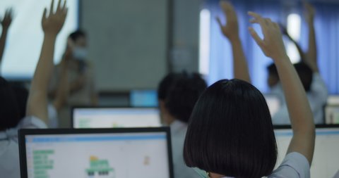 Slow motion of Asian high school students in white uniform actively study computer by raising their hands to answer questions on projector screen that teachers ask them  in computer classroom.