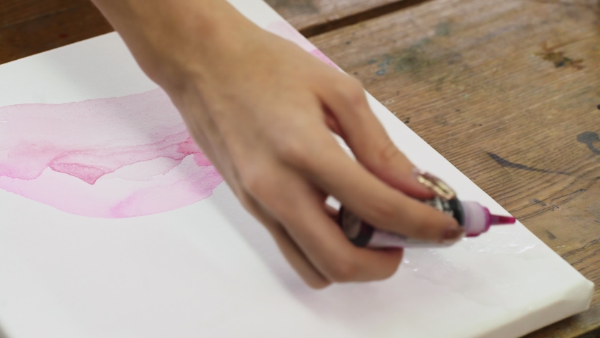 Close up of female artist paints an abstract picture, he uses pink paint fron tube on wet canves