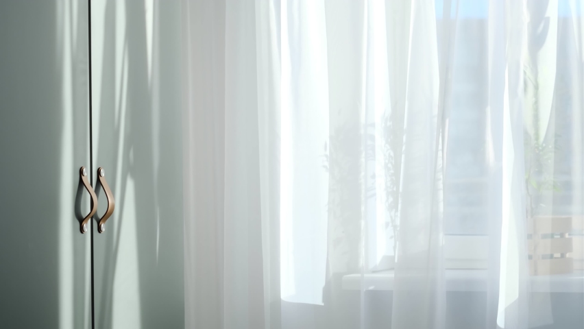 Bright morning sun in the open window through the curtains. Abstract white waving curtain in white bedroom apartment. Royalty-Free Stock Footage #1068969670