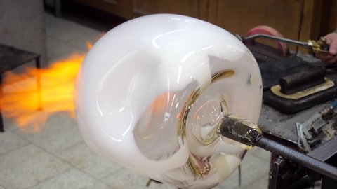 Glassblower forming big white bowl as semi product. Manual shaping hot glass in art studio. Man designer is creating a fluted square white bowl from this piece of molten glass.