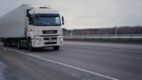 A truck is speeding along the Autobahn at great speed. A trucker is driving along the high-speed road. A large truck with a white body is driving along the Autobahn at high speed.