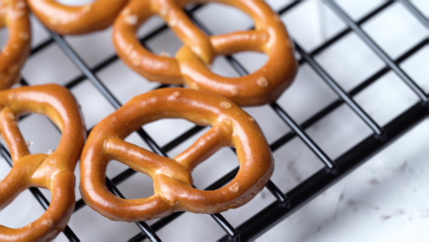 close up mini salted pretzels on wire cooling rack white background. hard crackers or snacks, dolly                             