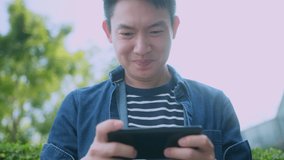 happiness adult mature asian male hand playing online game by smarthpone with fun and exited cheerful in outdoor garden after work leisure activity with smartphone technology cocnept