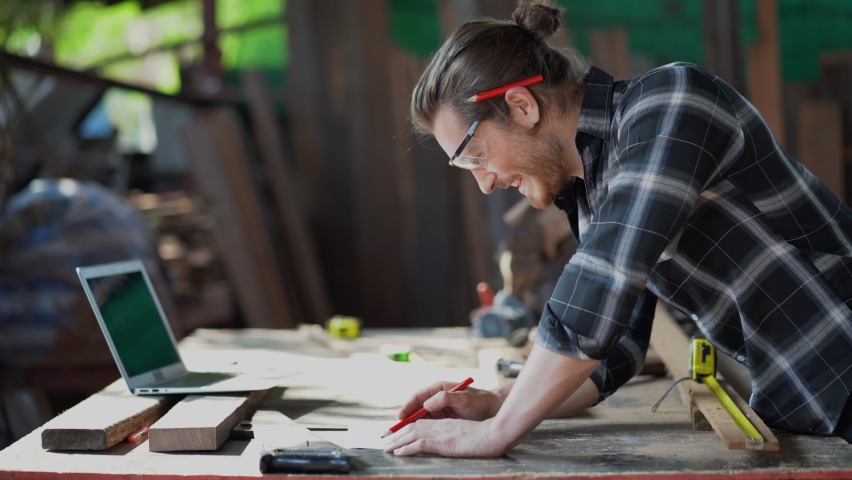 young hipster carpenter man working with computer laptop in workshop . craftsman wearing safety glasses checking order of clients or learning online Royalty-Free Stock Footage #1068988726