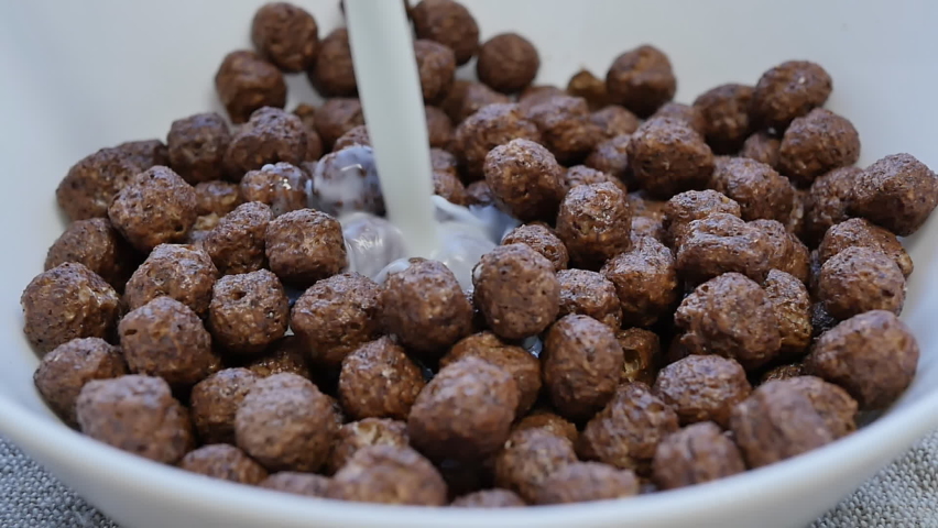 a stream of milk is poured into a bowl with dry and crunchy cocoa balls. Breakfast with healthy and wholesome food.
