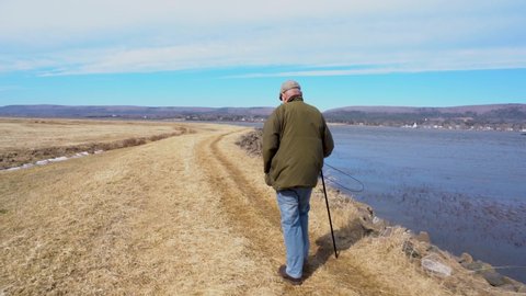 An older man walking with a painful limp on a coastal footpath in the winter.  Real person in pain with a real limp.