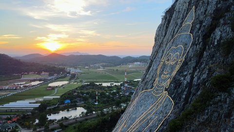 4k Aerial Medium shot Pan left at Buddha Mountain in Pattaya at Sunrise. Drone shot: image of Buddha engraved with gold into the hill in Khao Chi Chan, Chonburi, Thailand. Cinematic thai attractions.