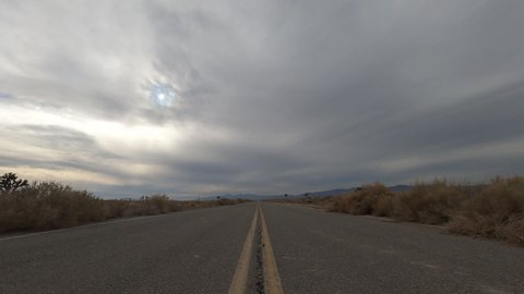 Looking down an empty road in the Mojave Desert with a stormy cloudscape overhead - low angle sunset time lapse