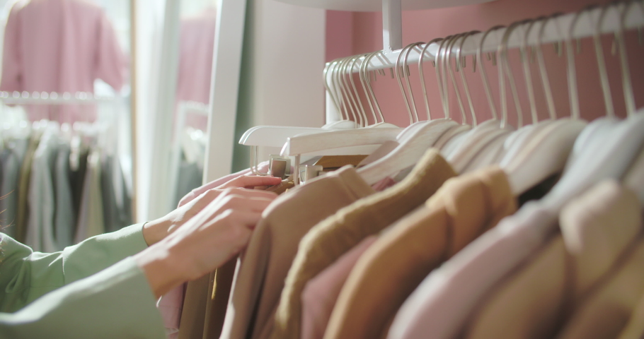 Close-up of Female Hands Plucked Hanger Choosing Clothes in a Clothing Store. Brunette Woman Hand Runs Across a Rack of Clothes Buying Clothes in a Shopping Mall. Sale Promotion and Shopping Concept. Royalty-Free Stock Footage #1069009456